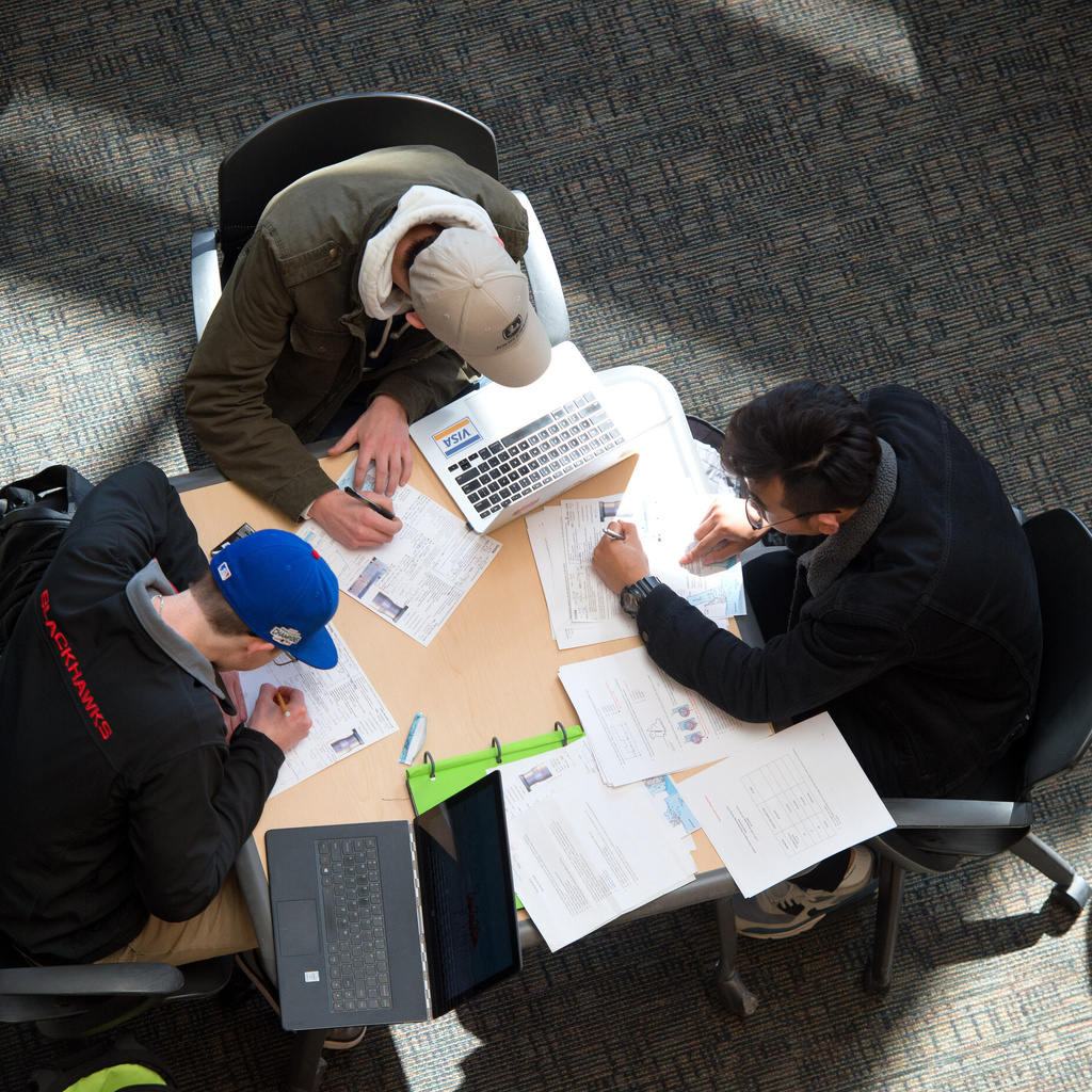 An aerial view of three students working on a multimedia project together at a table.